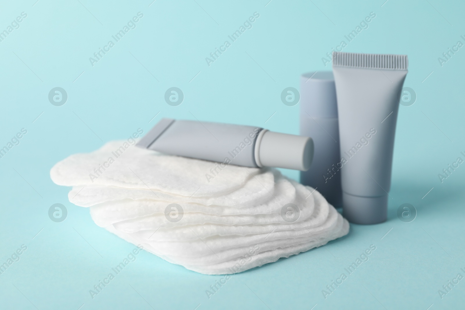 Photo of Clean cotton pads and cosmetic products on light blue background, closeup