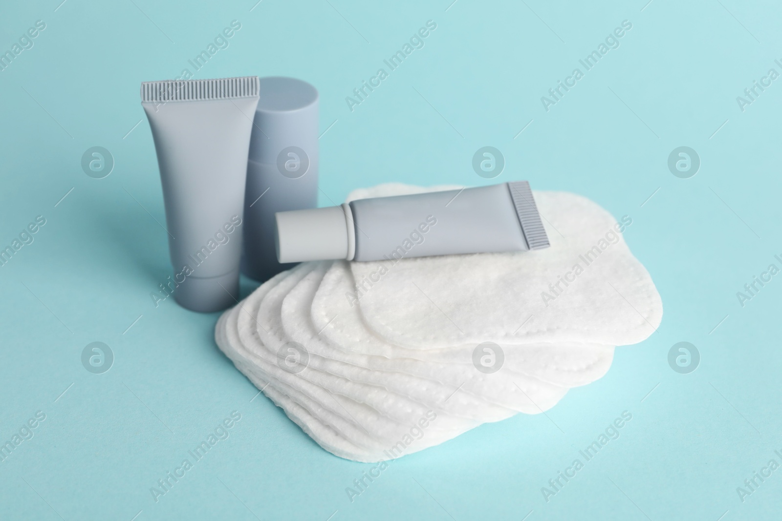 Photo of Clean cotton pads and cosmetic products on light blue background, closeup