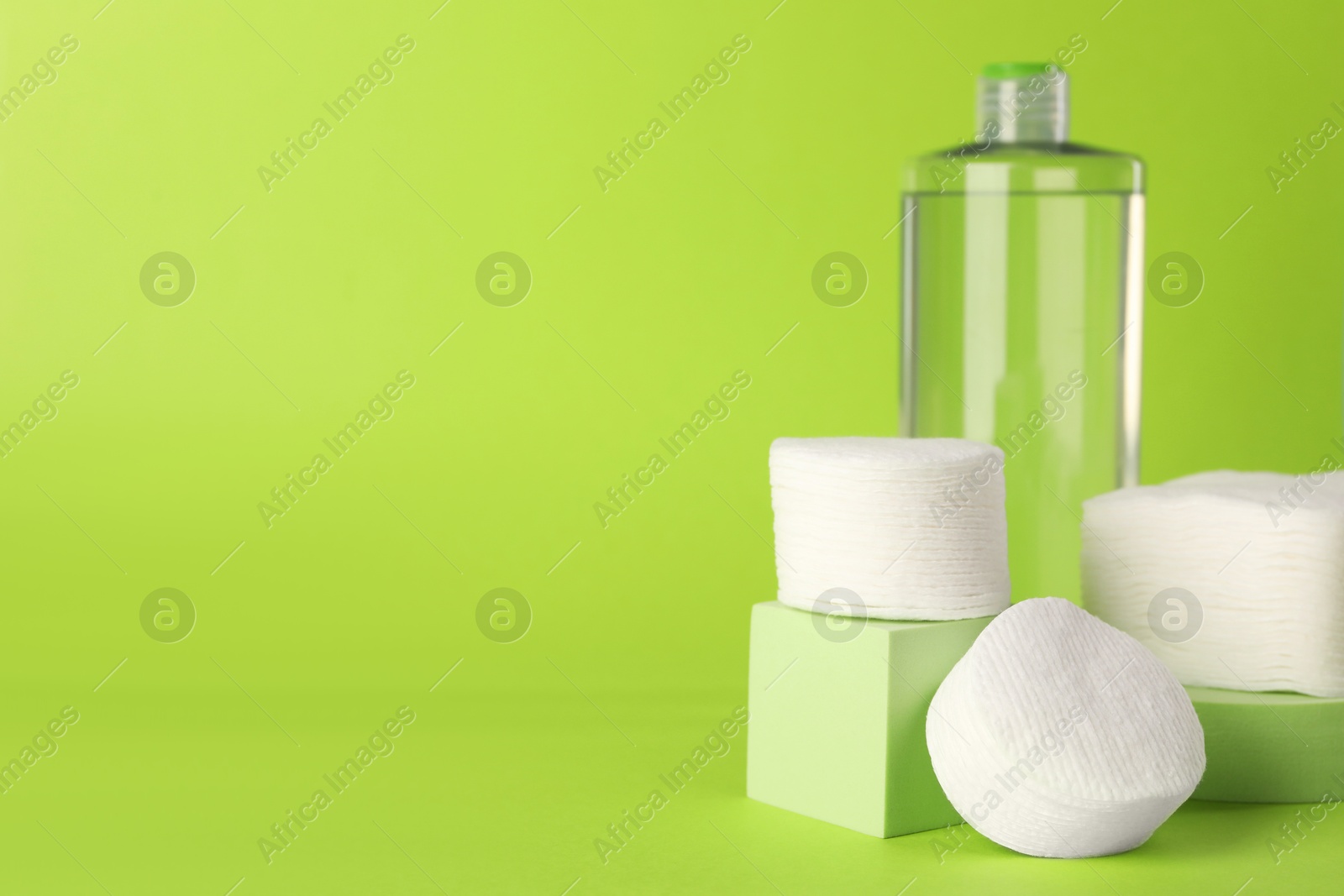 Photo of Clean cotton pads and micellar water on green background. Space for text