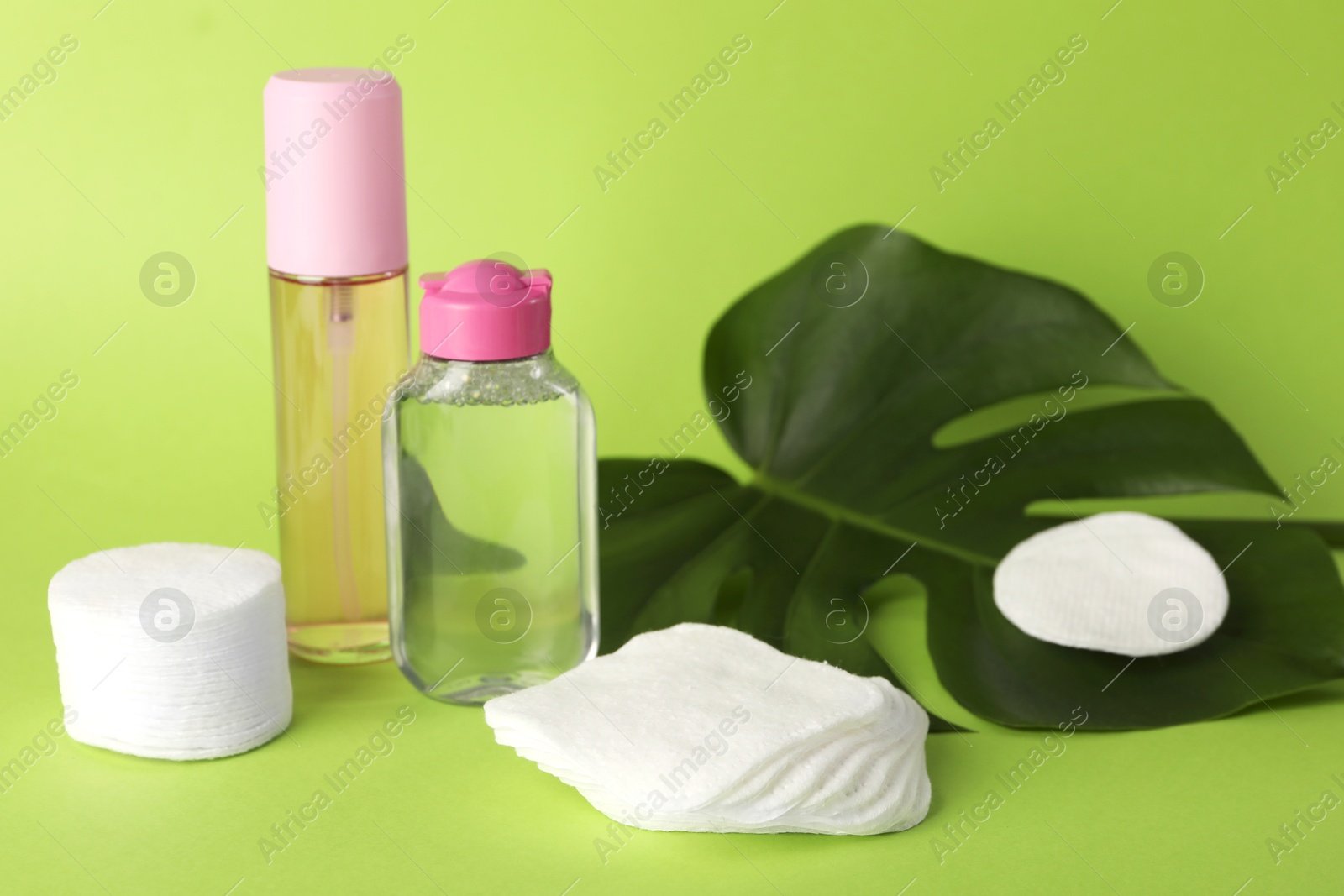 Photo of Clean cotton pads, cosmetic products and leaf on green background