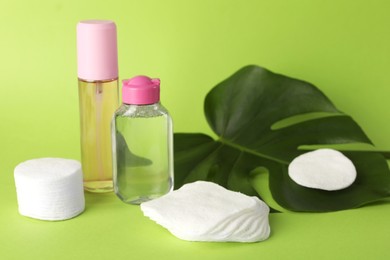 Photo of Clean cotton pads, cosmetic products and leaf on green background