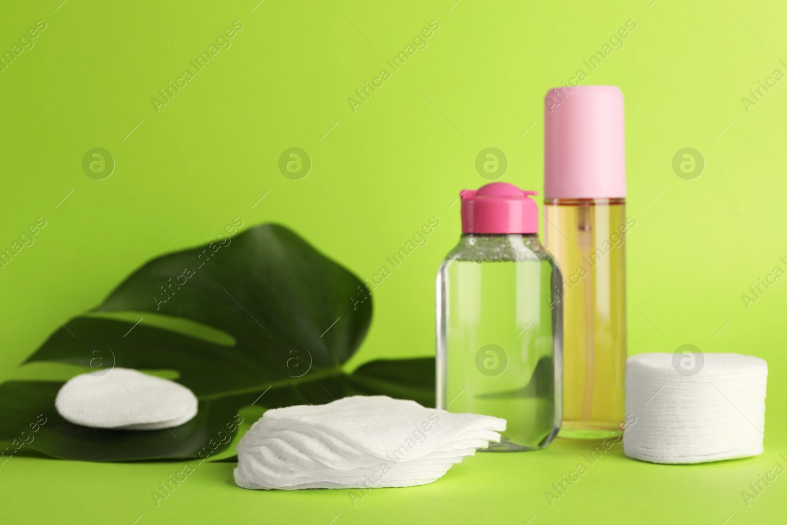 Photo of Clean cotton pads, cosmetic products and leaf on green background