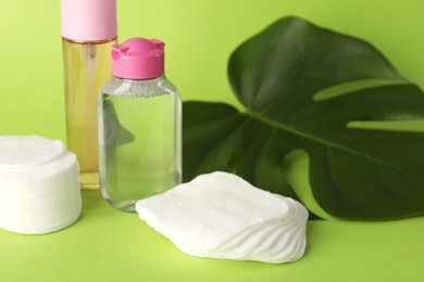 Photo of Clean cotton pads, cosmetic products and leaf on green background, closeup