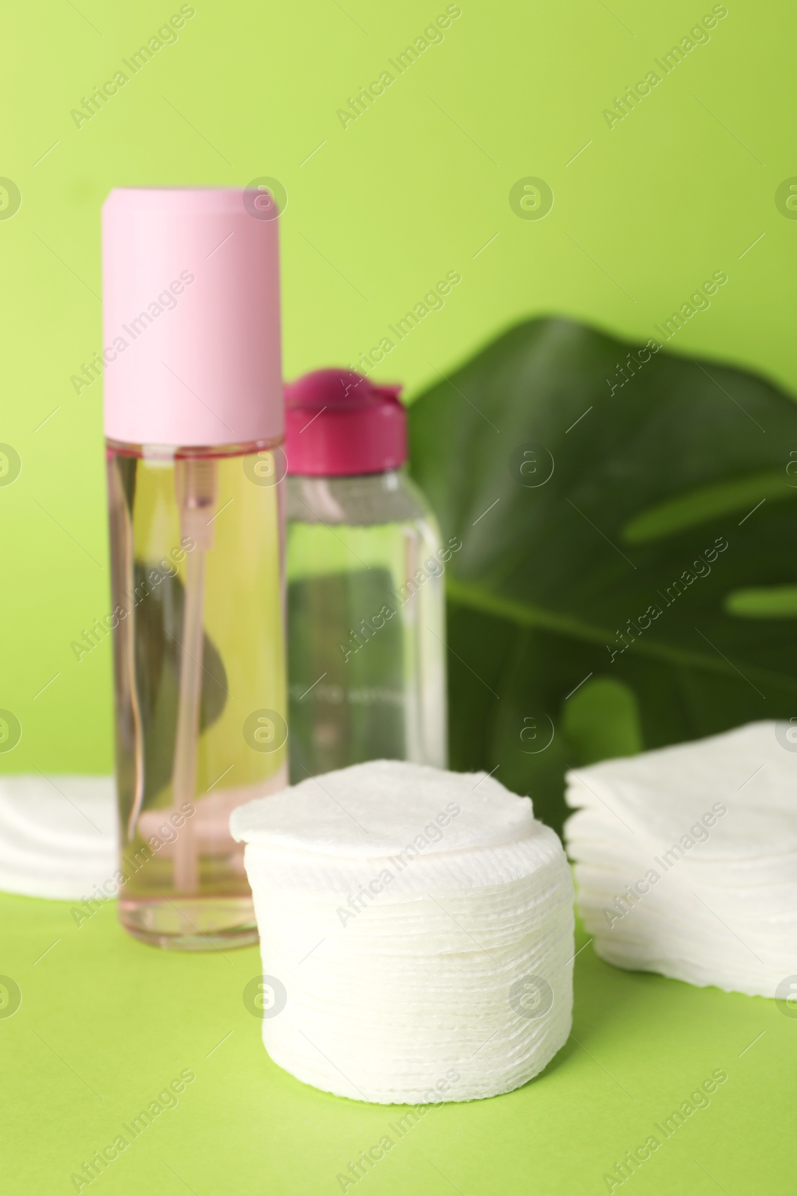 Photo of Clean cotton pads, cosmetic products and leaf on green background, closeup