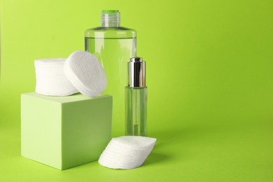 Photo of Clean cotton pads and cosmetic products on green background. Space for text