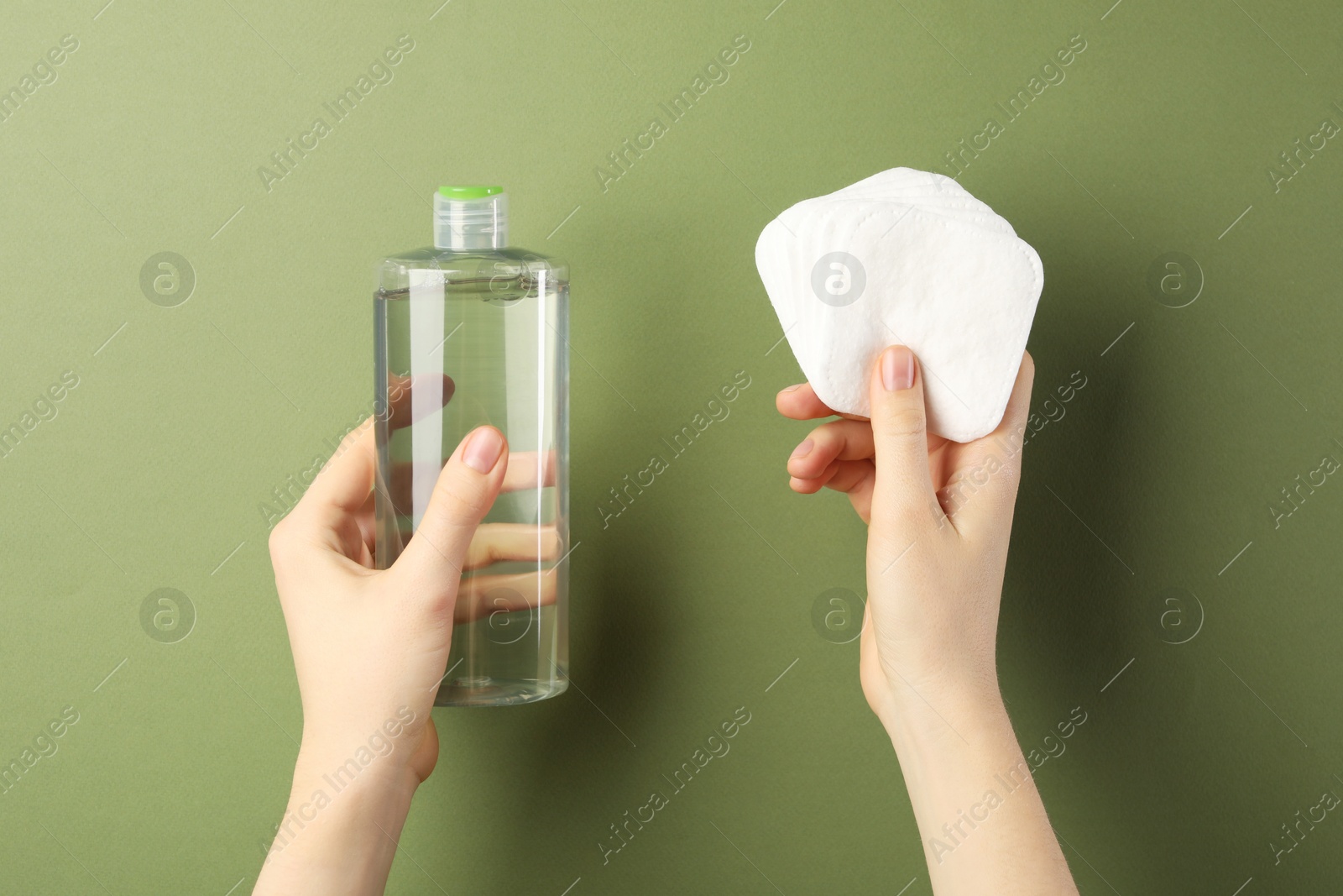 Photo of Woman with micellar water and clean cotton pads on olive background, closeup