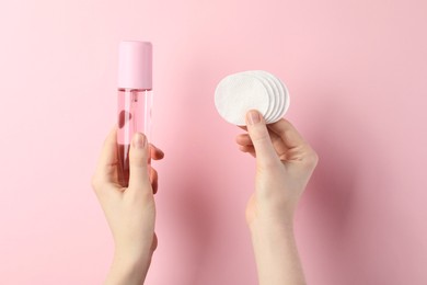 Photo of Woman with micellar water and clean cotton pads on light pink background, closeup