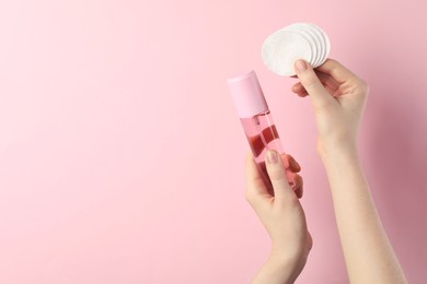 Photo of Woman with micellar water and clean cotton pads on light pink background, closeup. Space for text