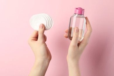 Photo of Woman with micellar water and clean cotton pads on light pink background, closeup