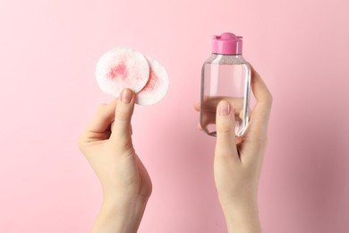 Photo of Woman with micellar water and dirty cotton pads on light pink background, closeup