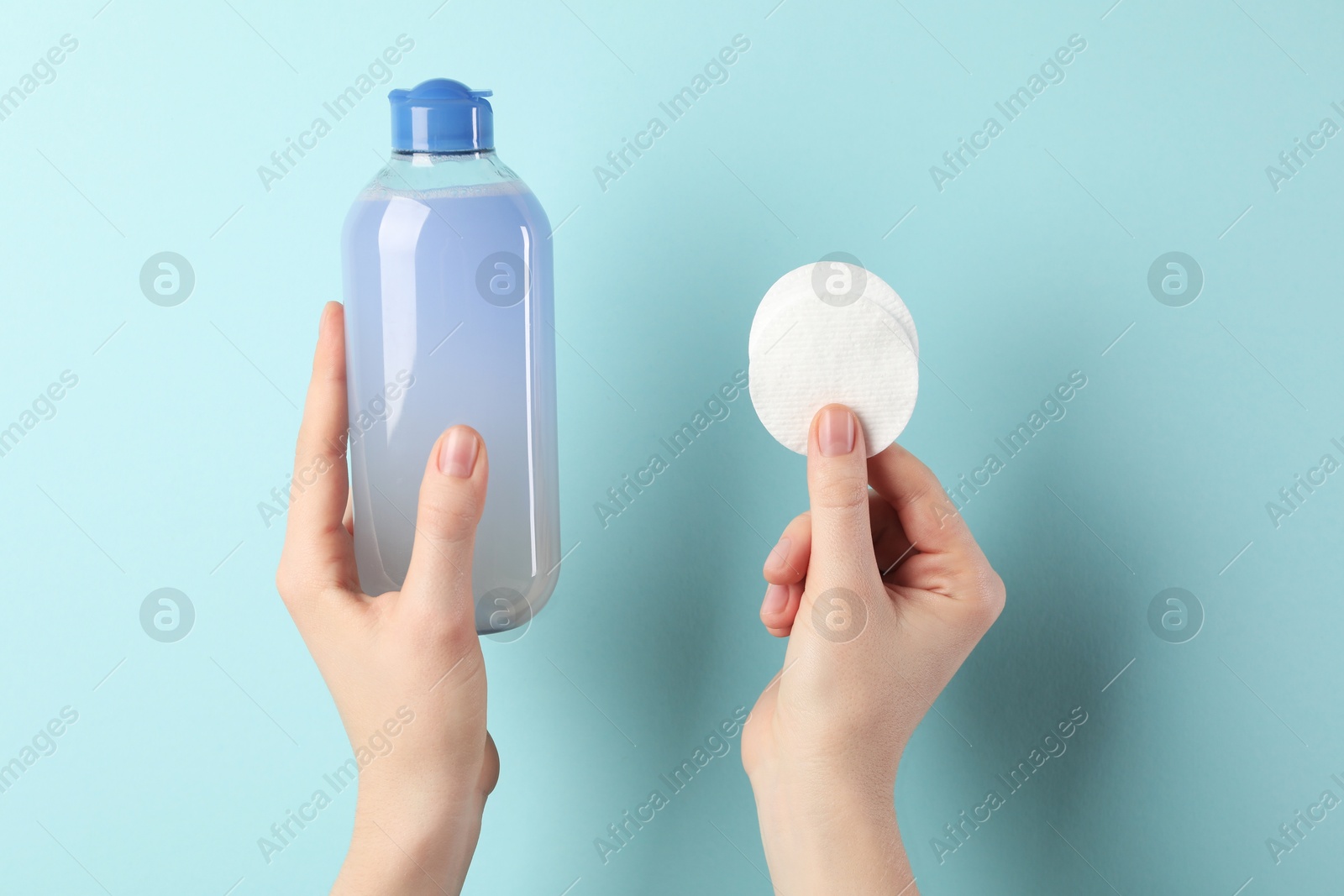 Photo of Woman with micellar water and clean cotton pads on light blue background, closeup