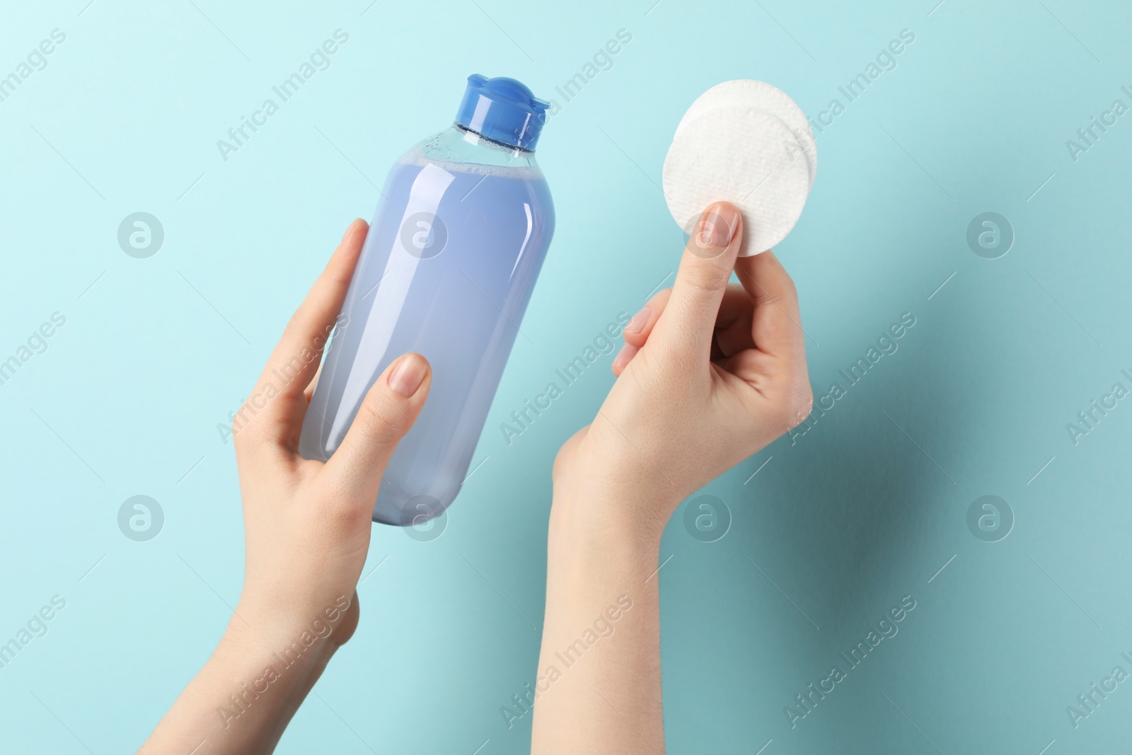 Photo of Woman with micellar water and clean cotton pads on light blue background, closeup