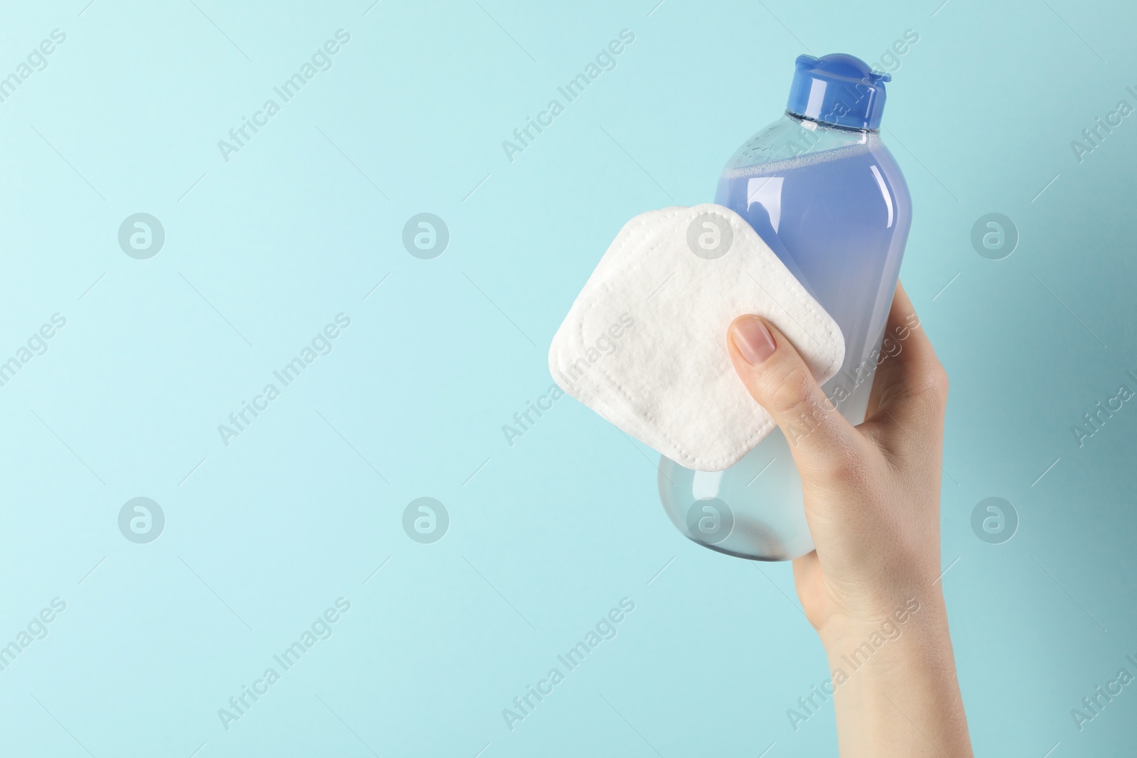 Photo of Woman with micellar water and clean cotton pads on light blue background, closeup. Space for text