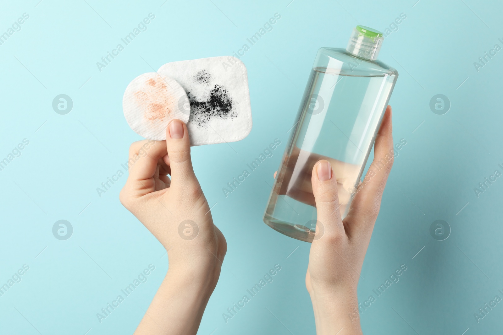 Photo of Woman with micellar water and dirty cotton pads on light blue background, closeup