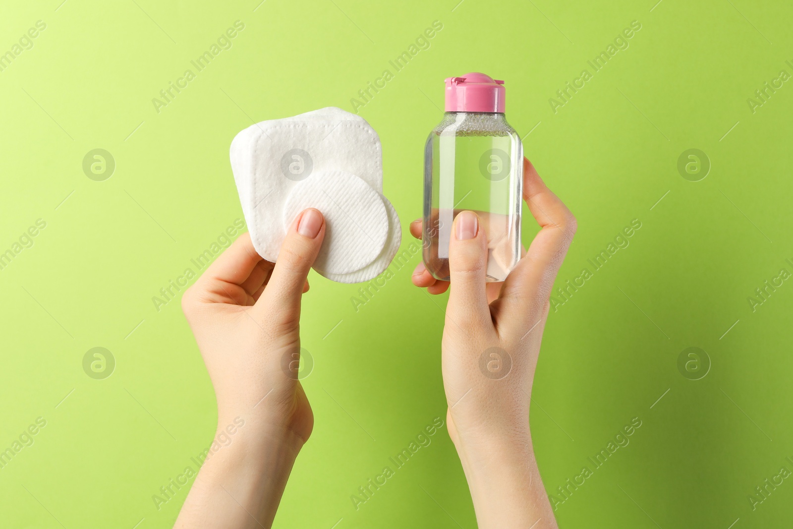 Photo of Woman with micellar water and clean cotton pads on green background, closeup