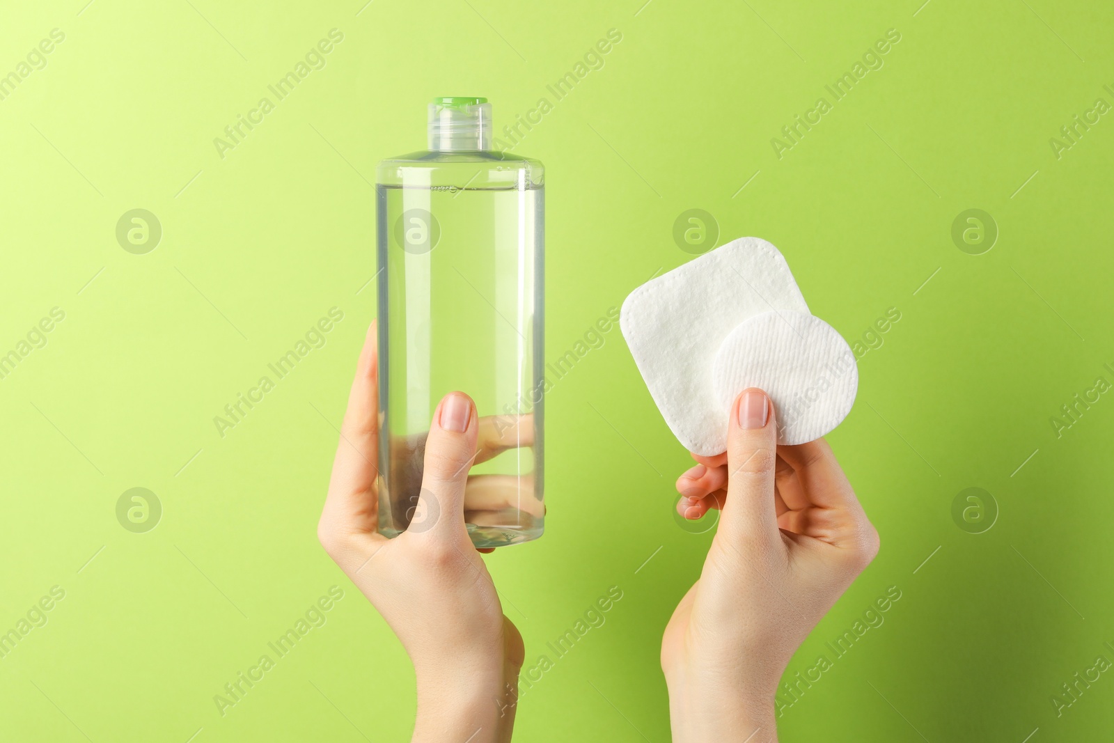 Photo of Woman with micellar water and clean cotton pads on green background, closeup