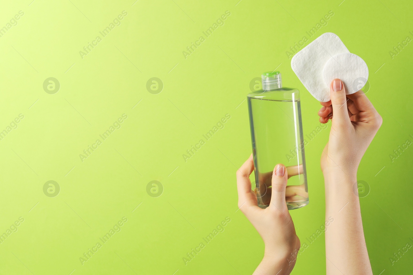 Photo of Woman with micellar water and clean cotton pads on green background, closeup. Space for text