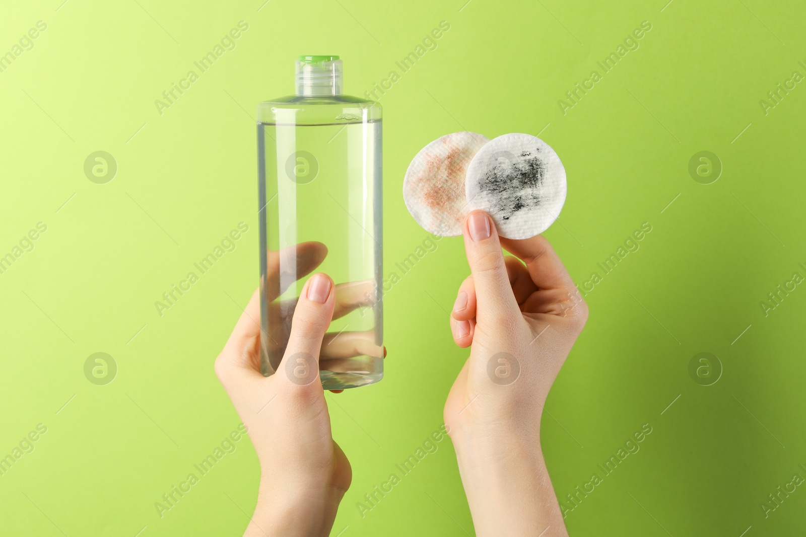 Photo of Woman with micellar water and dirty cotton pads on green background, closeup