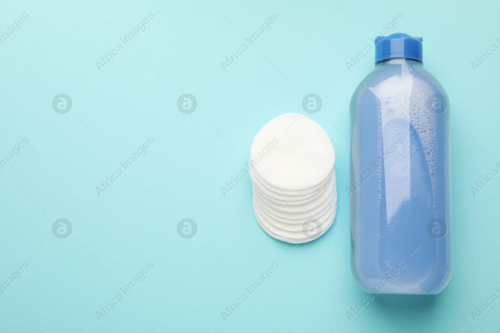 Photo of Clean cotton pads and micellar water on light blue background, top view. Space for text