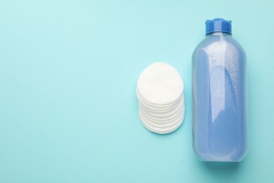 Photo of Clean cotton pads and micellar water on light blue background, top view. Space for text