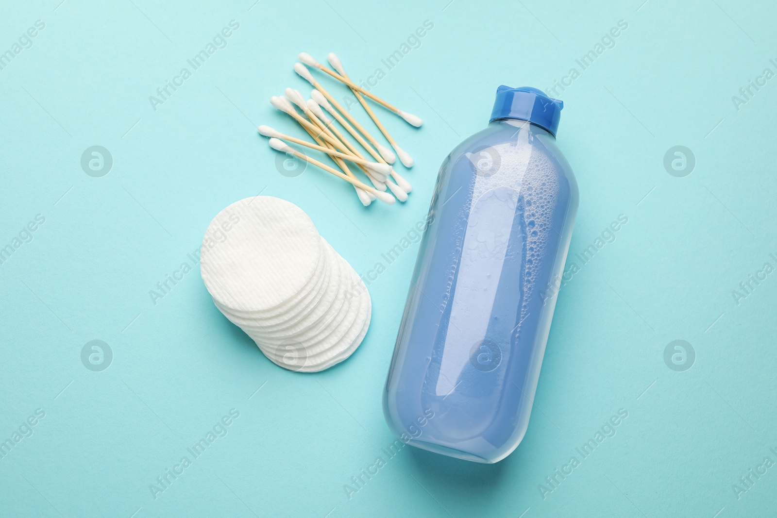 Photo of Clean cotton pads, swabs and micellar water on light blue background, flat lay