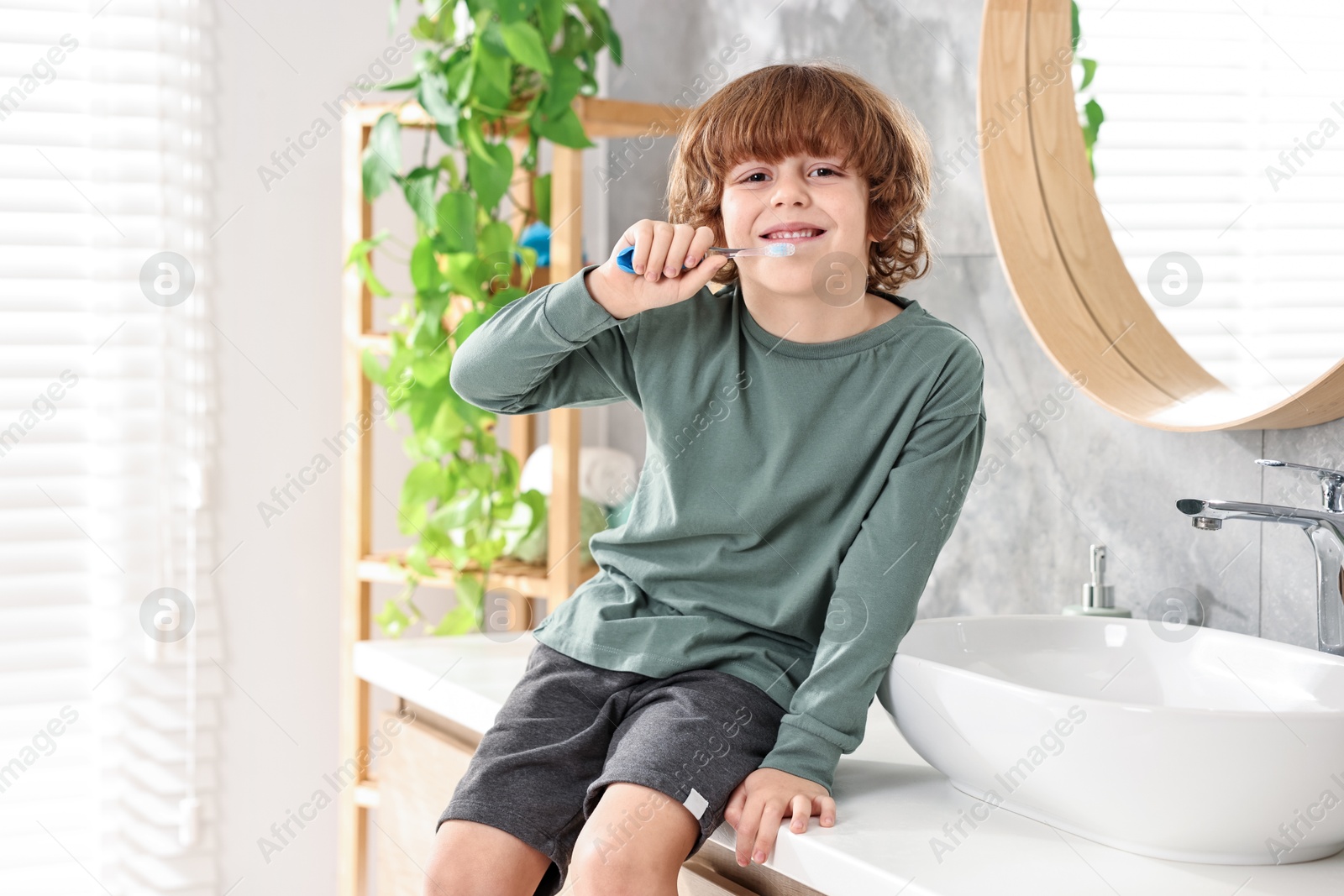 Photo of Cute boy brushing his teeth on countertop in bathroom