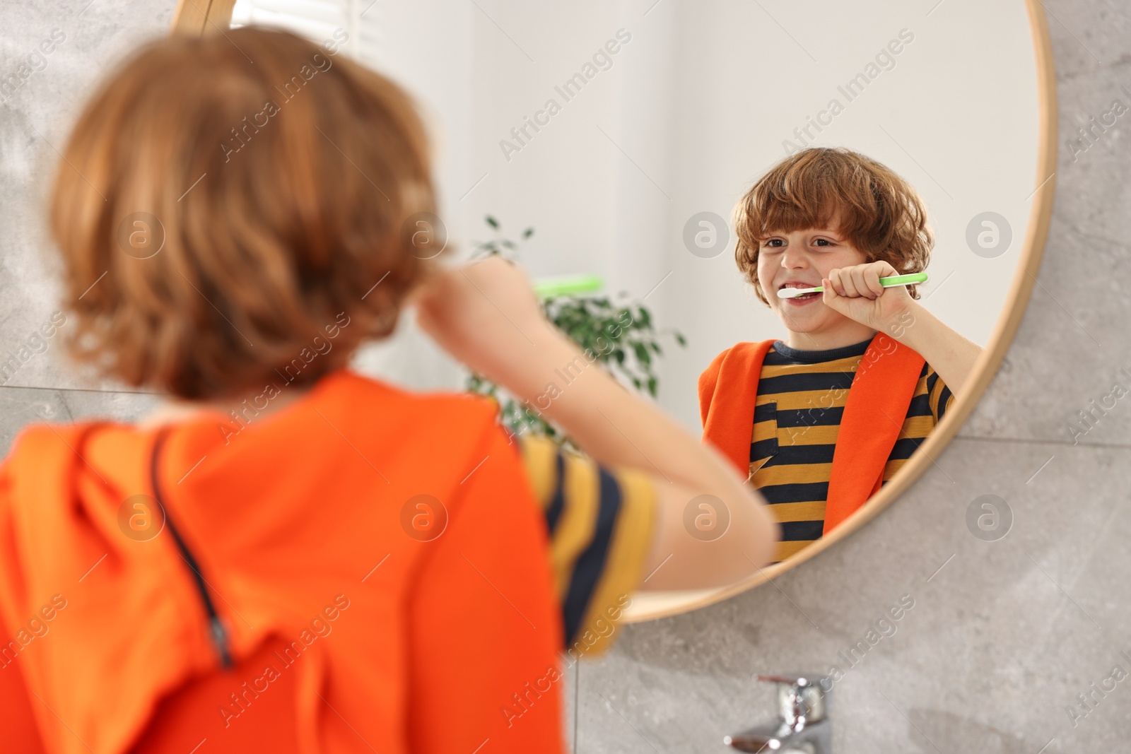 Photo of Cute boy brushing his teeth near mirror in bathroom, selective focus