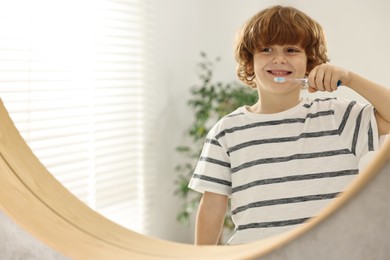 Photo of Cute boy brushing his teeth near mirror indoors