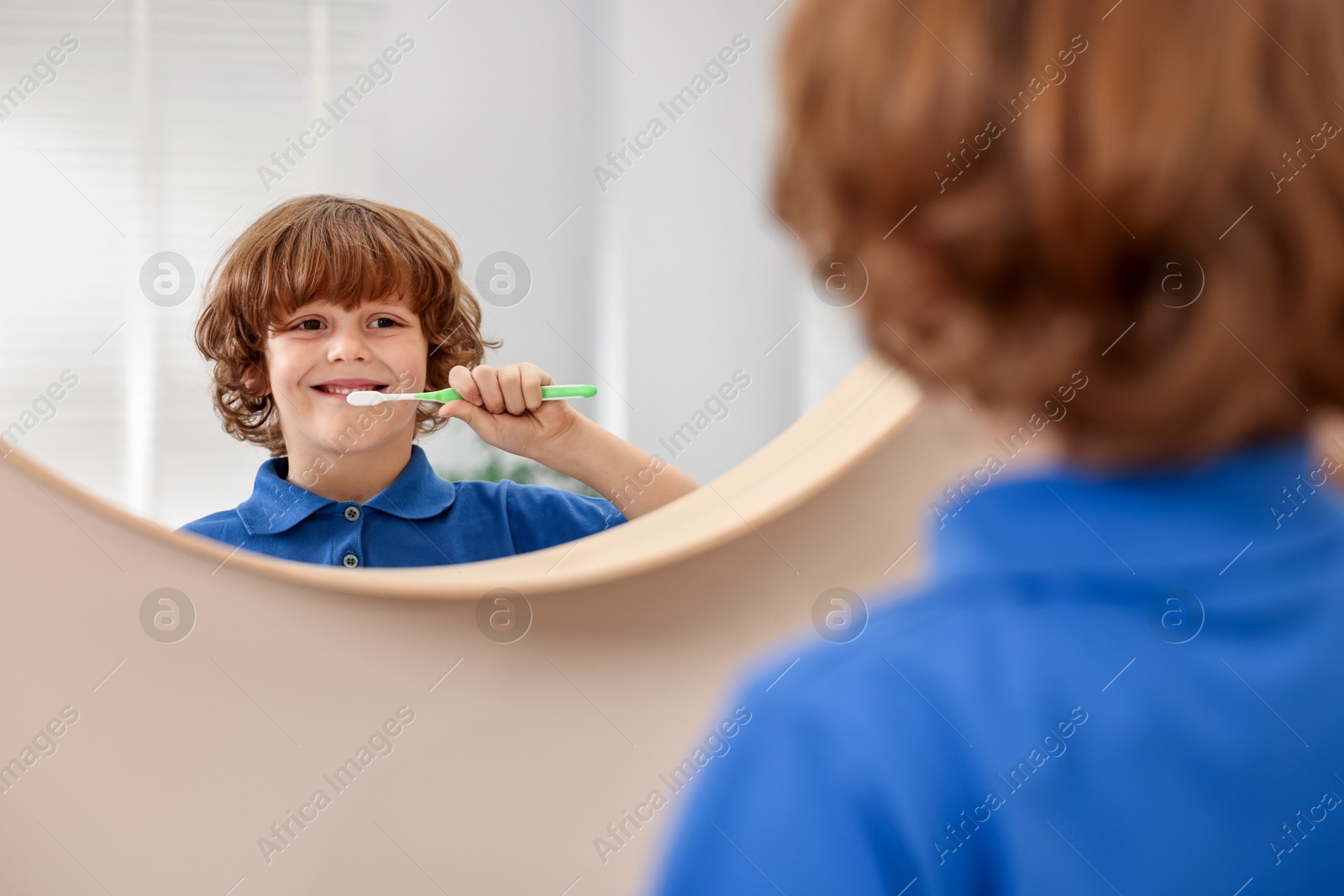 Photo of Cute boy brushing his teeth near mirror at home, selective focus