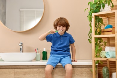 Photo of Cute boy brushing his teeth on countertop in bathroom