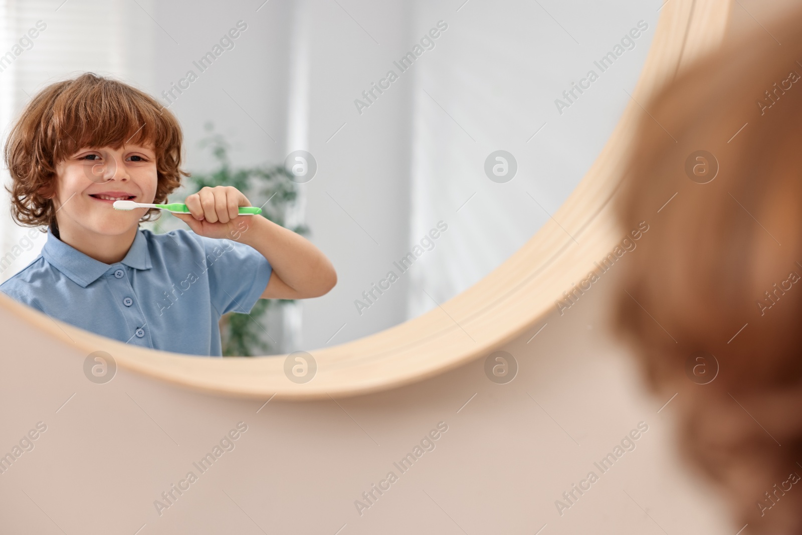 Photo of Cute boy brushing his teeth near mirror at home, selective focus