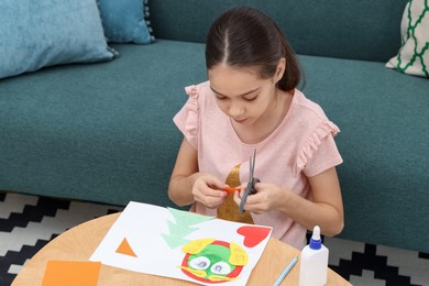 Photo of Girl cutting figure out of color paper for her creative project at home. Art and craft