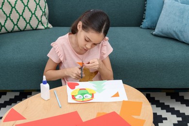 Photo of Girl cutting figure out of color paper for her creative project at home. Art and craft