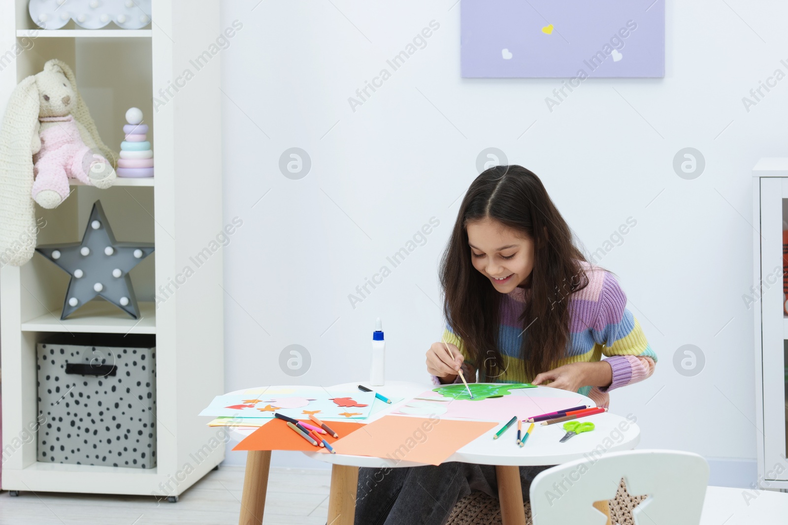 Photo of Girl applying glue onto paper figure for her creative project at table indoors, space for text. Art and craft