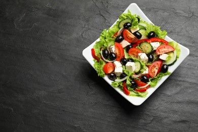 Photo of Delicious fresh Greek salad on black table, top view. Space for text