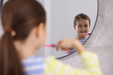 Photo of Cute girl brushing her teeth near mirror in bathroom, selective focus