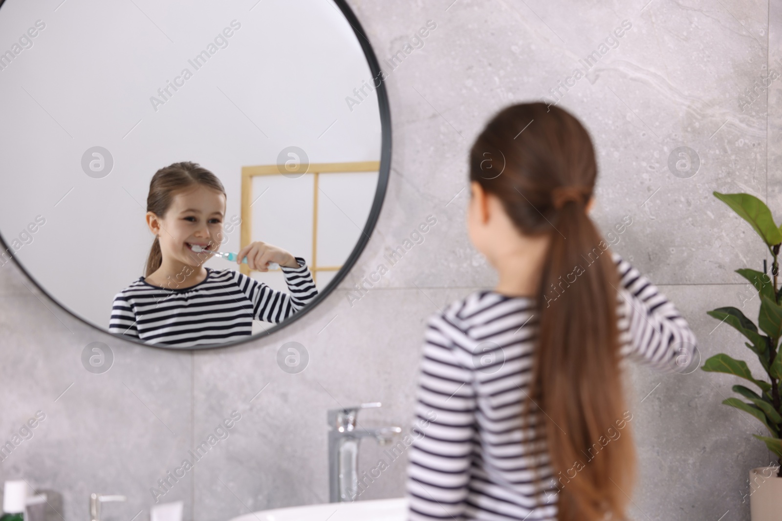 Photo of Cute girl brushing her teeth near mirror in bathroom, selective focus