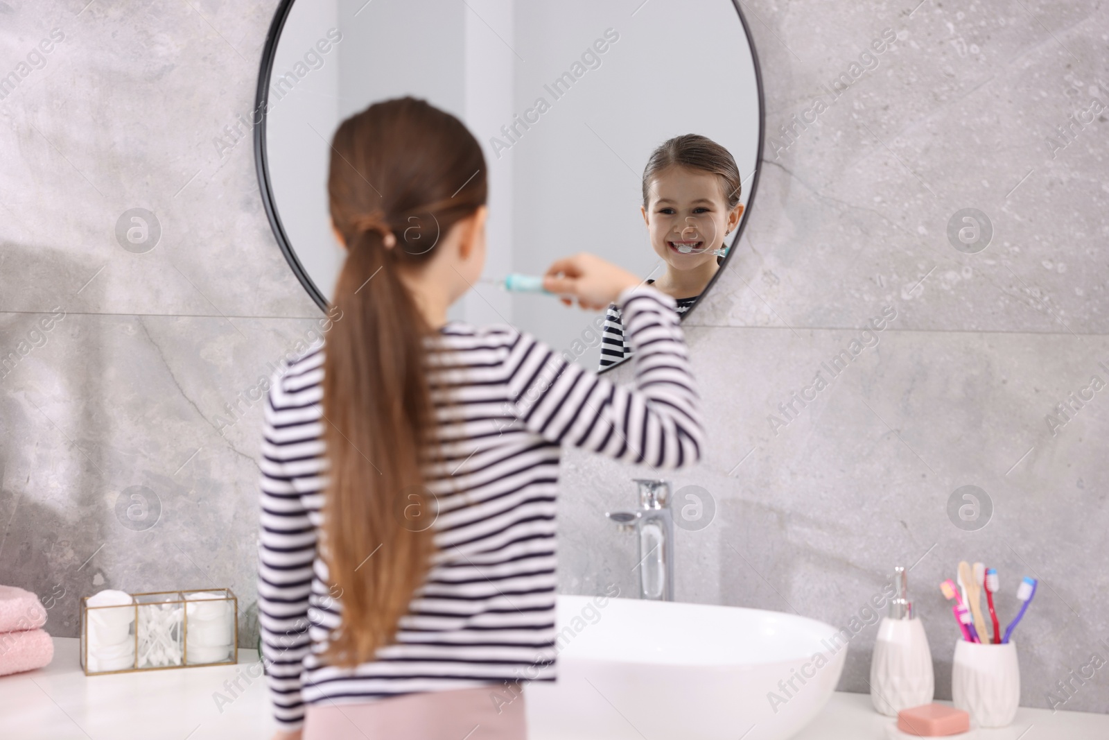 Photo of Cute girl brushing her teeth near mirror in bathroom, selective focus