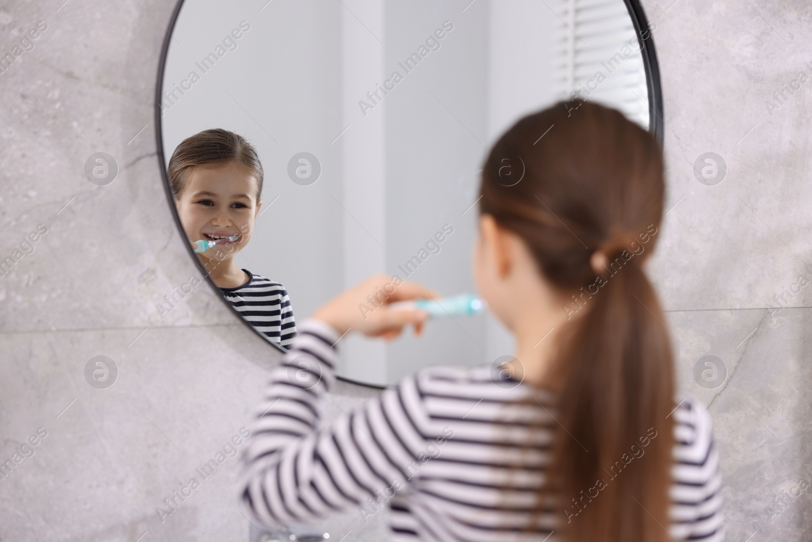 Photo of Cute girl brushing her teeth near mirror in bathroom, selective focus