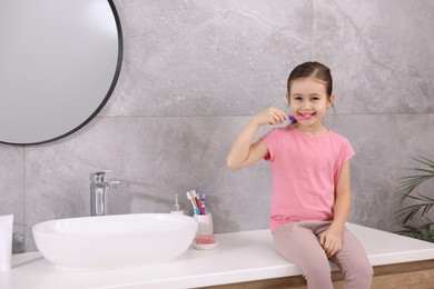 Photo of Cute girl brushing her teeth on countertop in bathroom