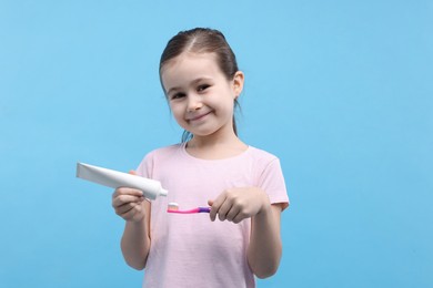 Photo of Cute girl applying toothpaste onto toothbrush on light blue background