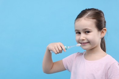 Photo of Cute girl with toothbrush on light blue background, space for text