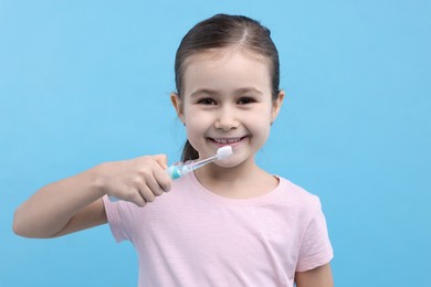 Photo of Cute girl with toothbrush on light blue background