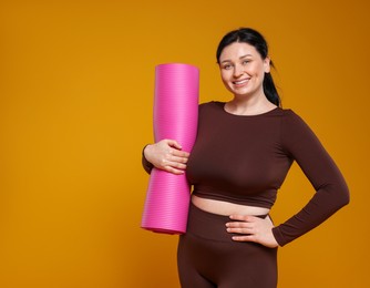 Photo of Plus size woman in gym clothes with fitness mat on orange background, space for text