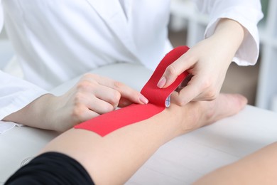 Photo of Doctor applying kinesio tapes to patient's foot in hospital, closeup