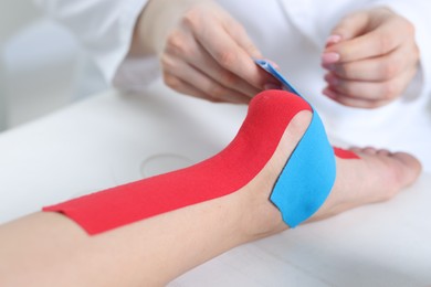 Photo of Doctor applying kinesio tapes to patient's foot in hospital, closeup