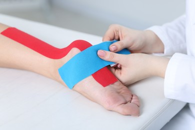 Photo of Doctor applying kinesio tapes to patient's foot in hospital, closeup