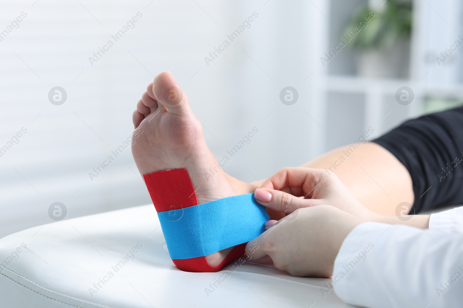 Photo of Doctor applying kinesio tapes to patient's foot in hospital, closeup