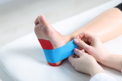 Photo of Doctor applying kinesio tapes to patient's foot in hospital, closeup