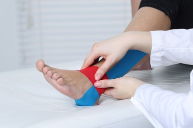 Photo of Doctor applying kinesio tapes to patient's foot in hospital, closeup